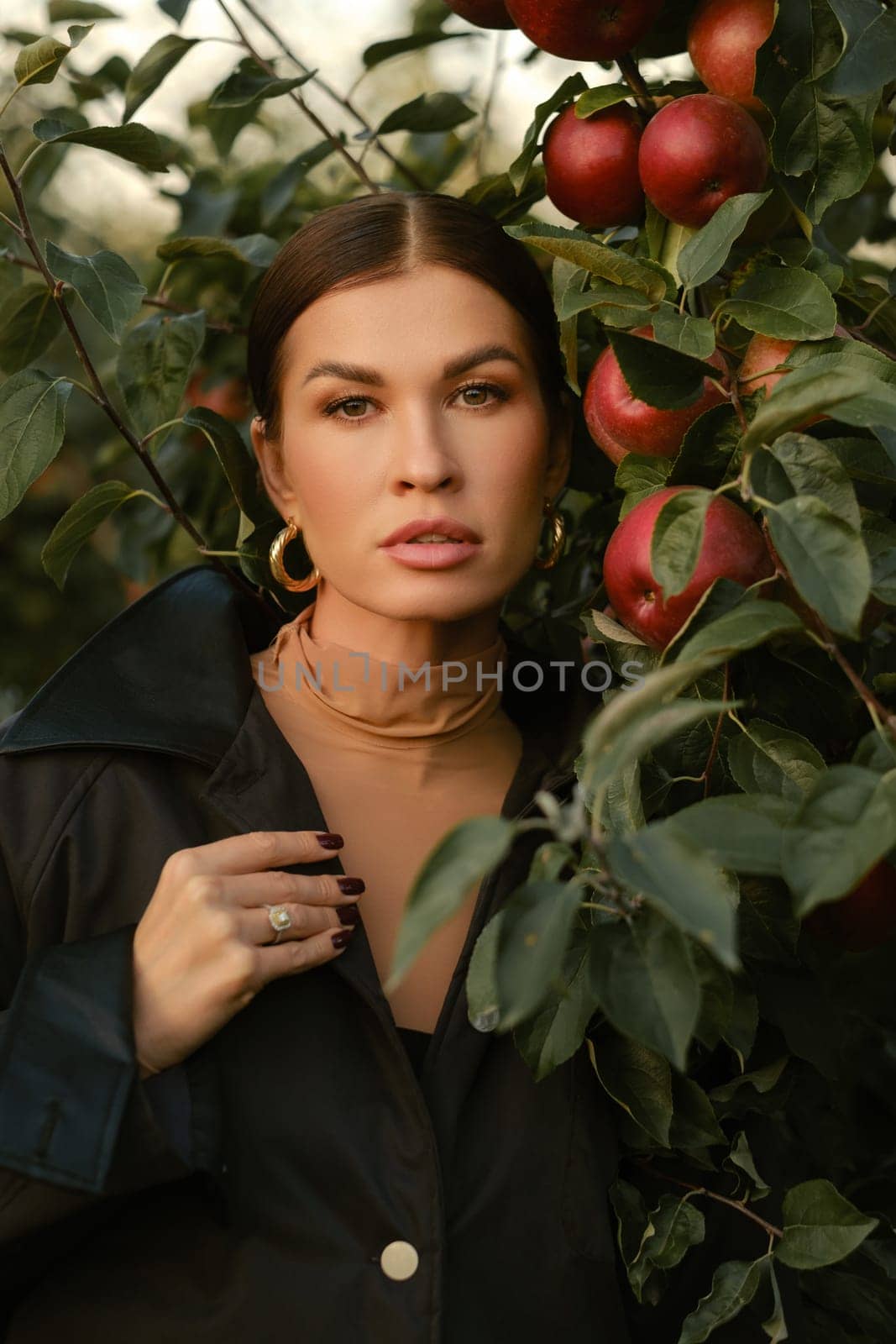 A beautiful girl in a black autumn jacket in an apple orchard. A fashionable girl at a fashion show in the apple orchard.