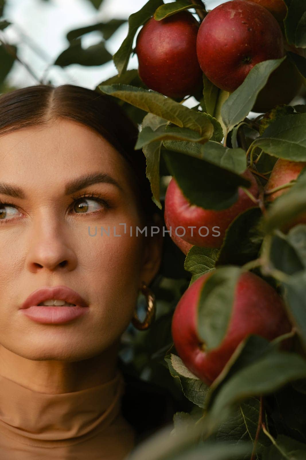 Close-up of a girl's face in an apple orchard. A fashionable girl on the background of a tree with red apples.