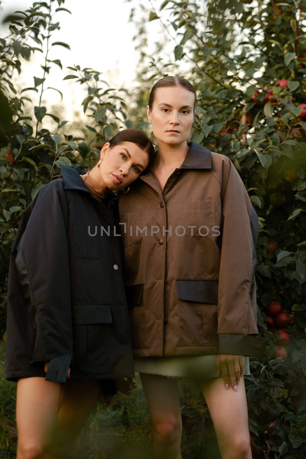 Two stylish girls in jackets at a fashion show in the apple orchard. Fashion show in the garden.