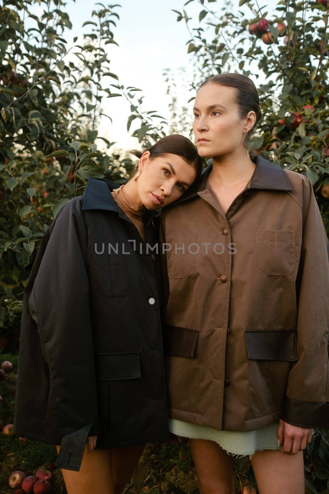Two stylish girls in jackets at a fashion show in the apple orchard. Fashion show in the garden.