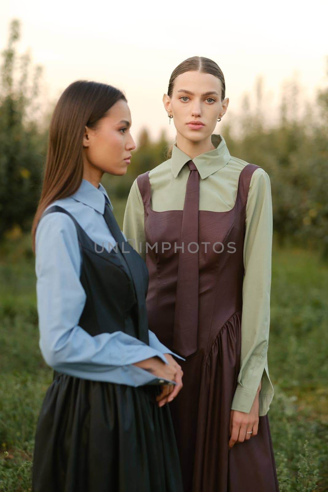 Two stylish girls in dresses with ties in the summer garden. Fashion show in nature.