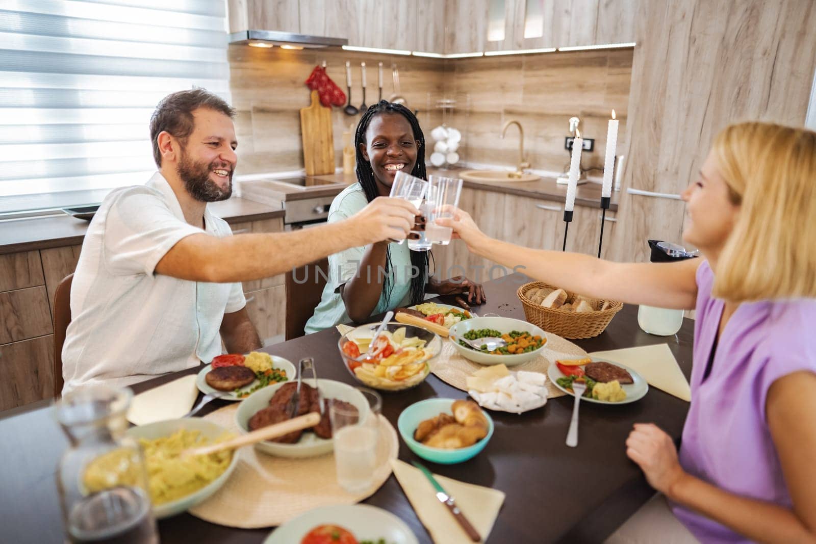 Three friends toast with drinks around a table full of delicious food.