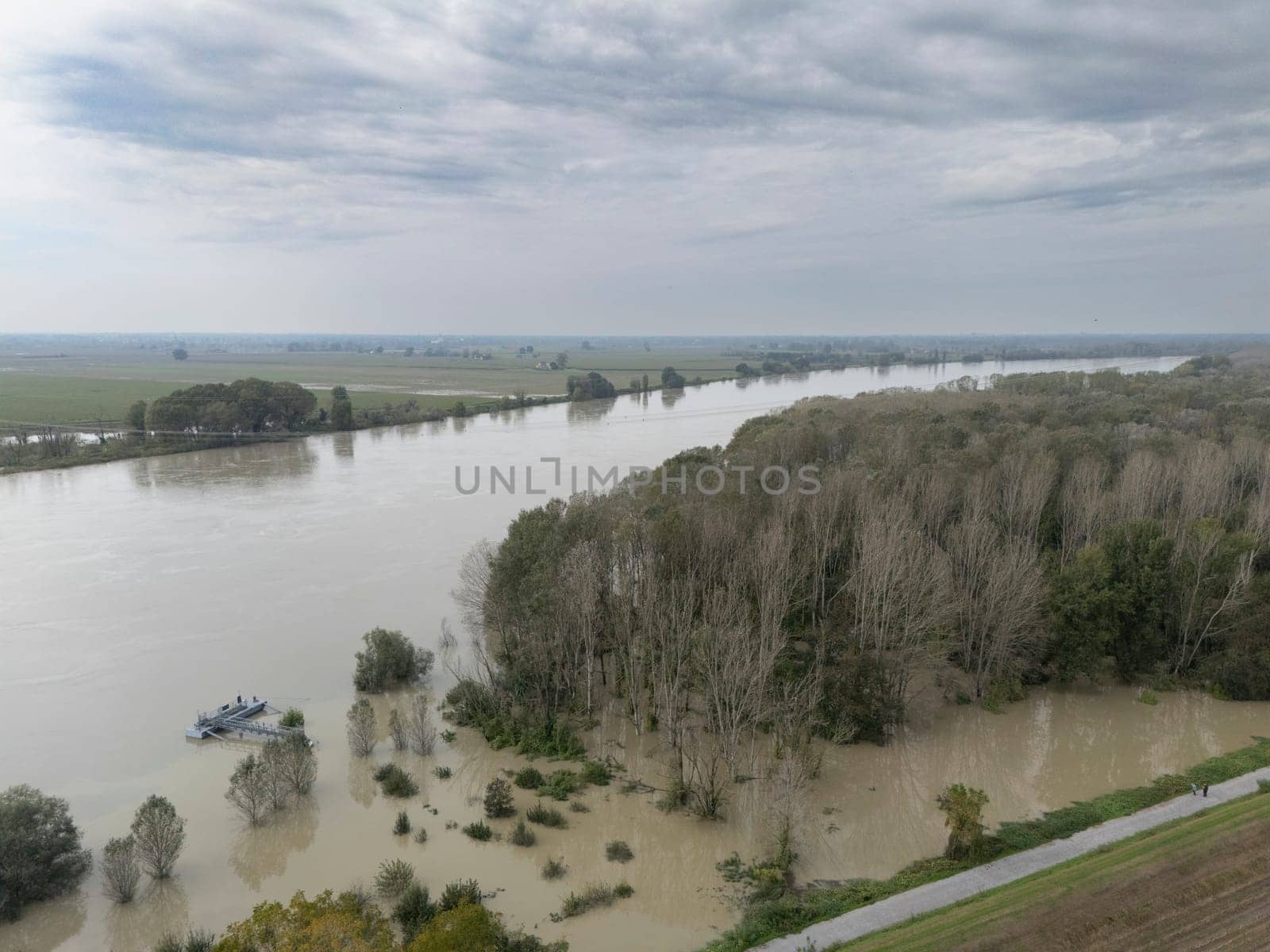 Stagno Lombardo, Italy - October 20th 2024 Aerial view of a river flooding the surrounding fields and forests after a heavy rain period, with the cloudy sky in the background