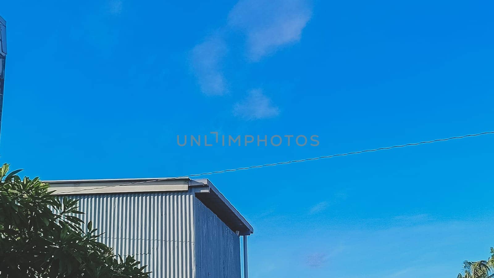 A warehouse and a tree under the blue sky. The warehouse placed beside a tree. The warehouse and the tree shined by the sun.
