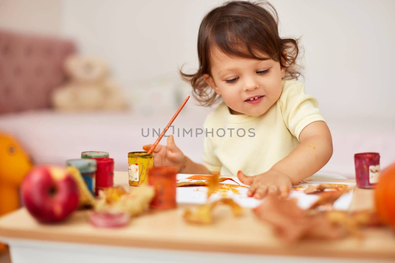 smiling little child girl painting her hands and autumn leaves. baby girl drawing hands in yellow paint