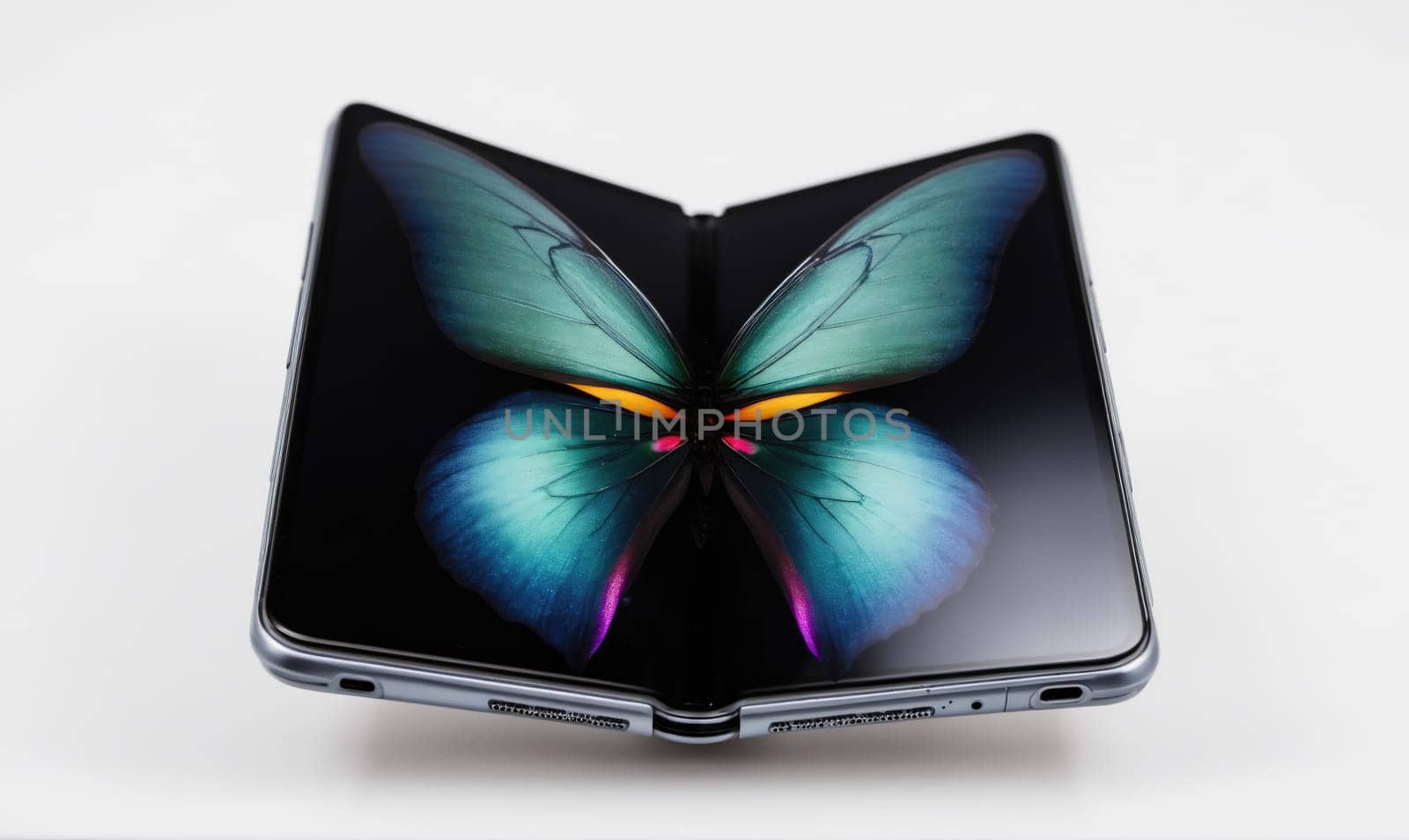 A gray foldable smartphone with a black screen is unfolded and laying on a white surface. The screen is displaying a blue butterfly with yellow accents.