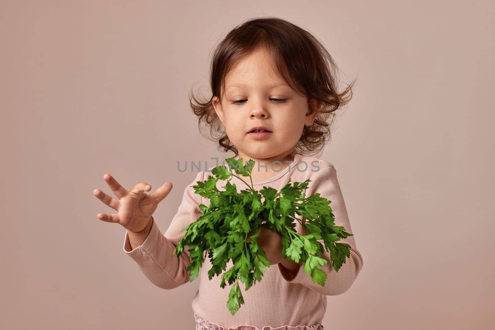little child girl with fresh green parsley on beige background. healthy baby food.