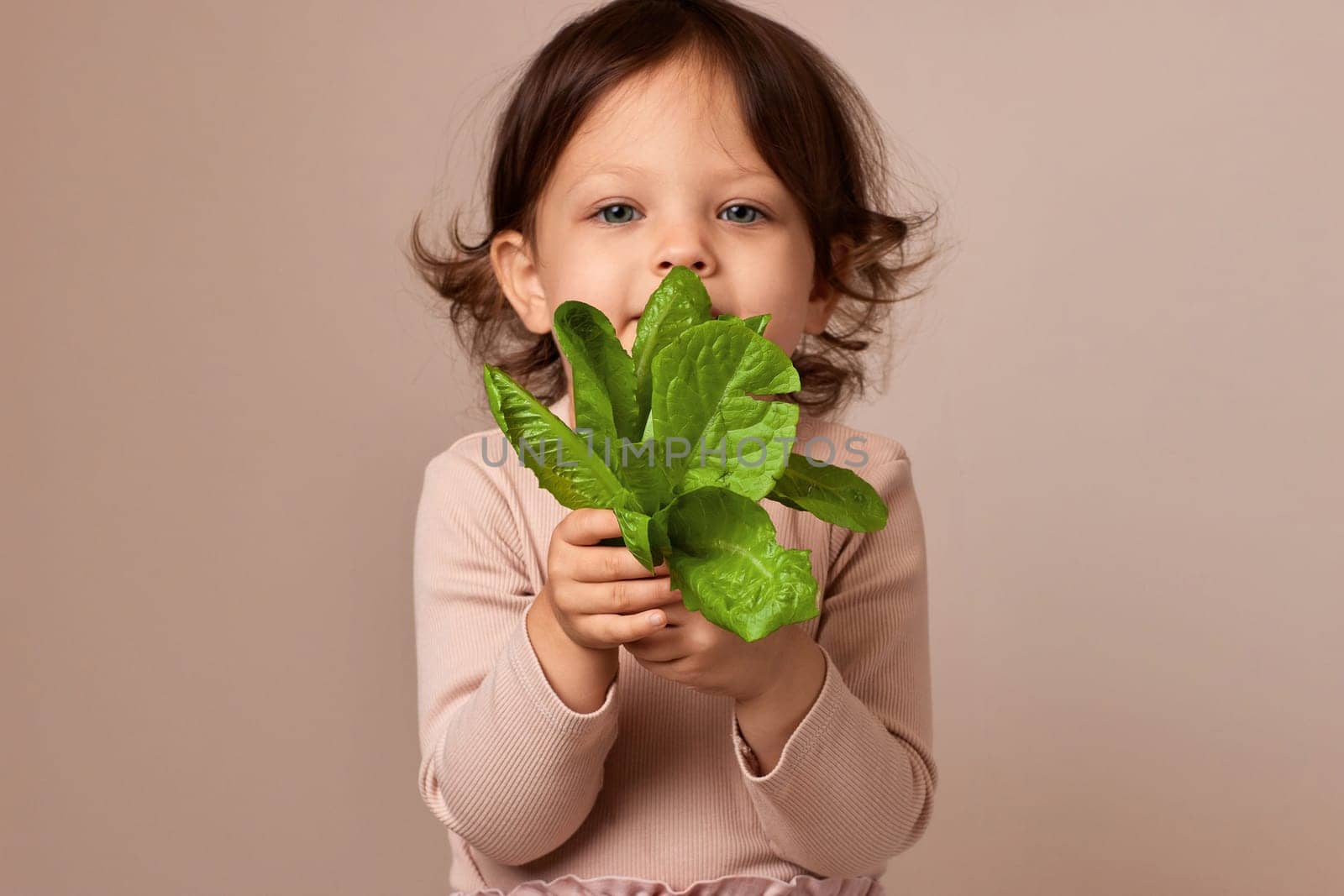 smiling child girl holding fresh green salad on beige background. focus on salad