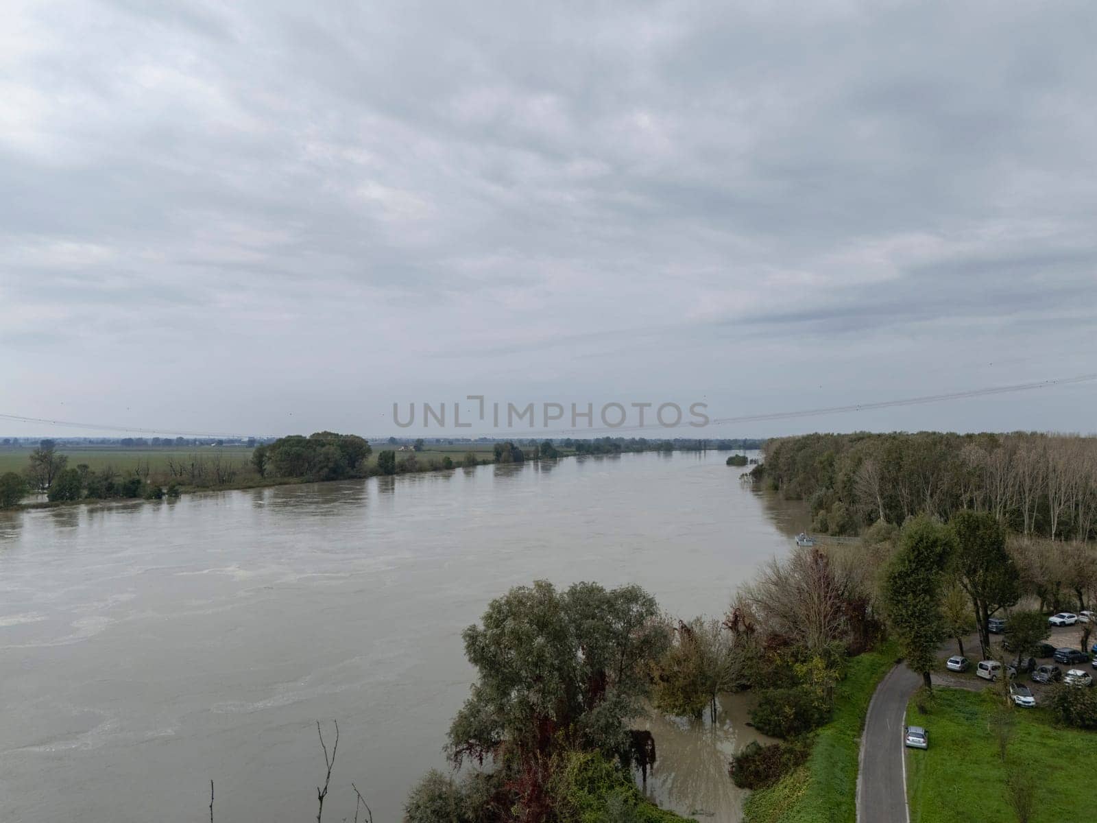 Stagno Lombardo, Italy - October 20th 2024 Aerial view of a river flooding the surrounding fields and forests after a heavy rain period, with the cloudy sky in the background