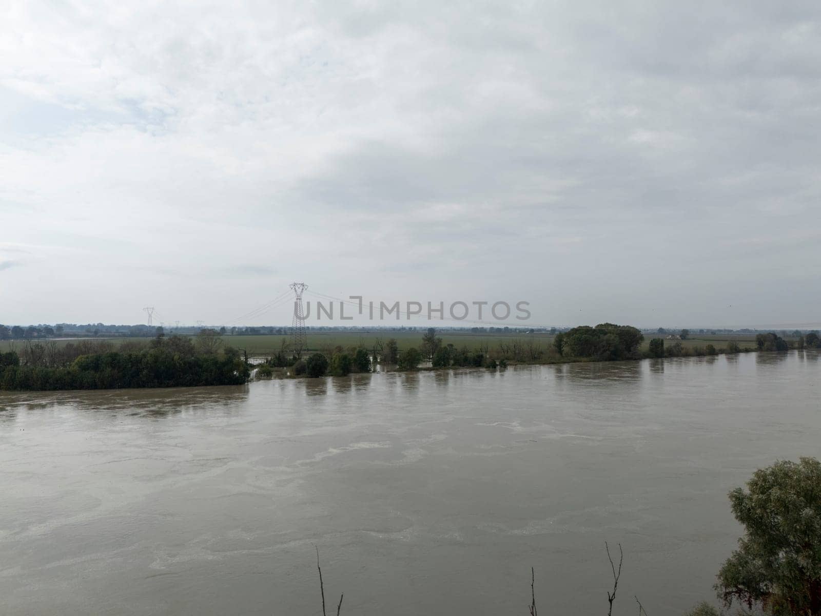 Stagno Lombardo, Italy - October 20th 2024 Aerial view of a river flooding the surrounding fields and forests after a heavy rain period, with the cloudy sky in the background