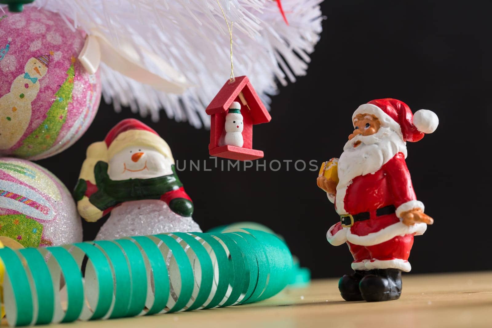 A small figurine of Santa Claus in a red and white suit holding a green sack, set against a blurred background. This festive ornament captures the spirit of Christmas.