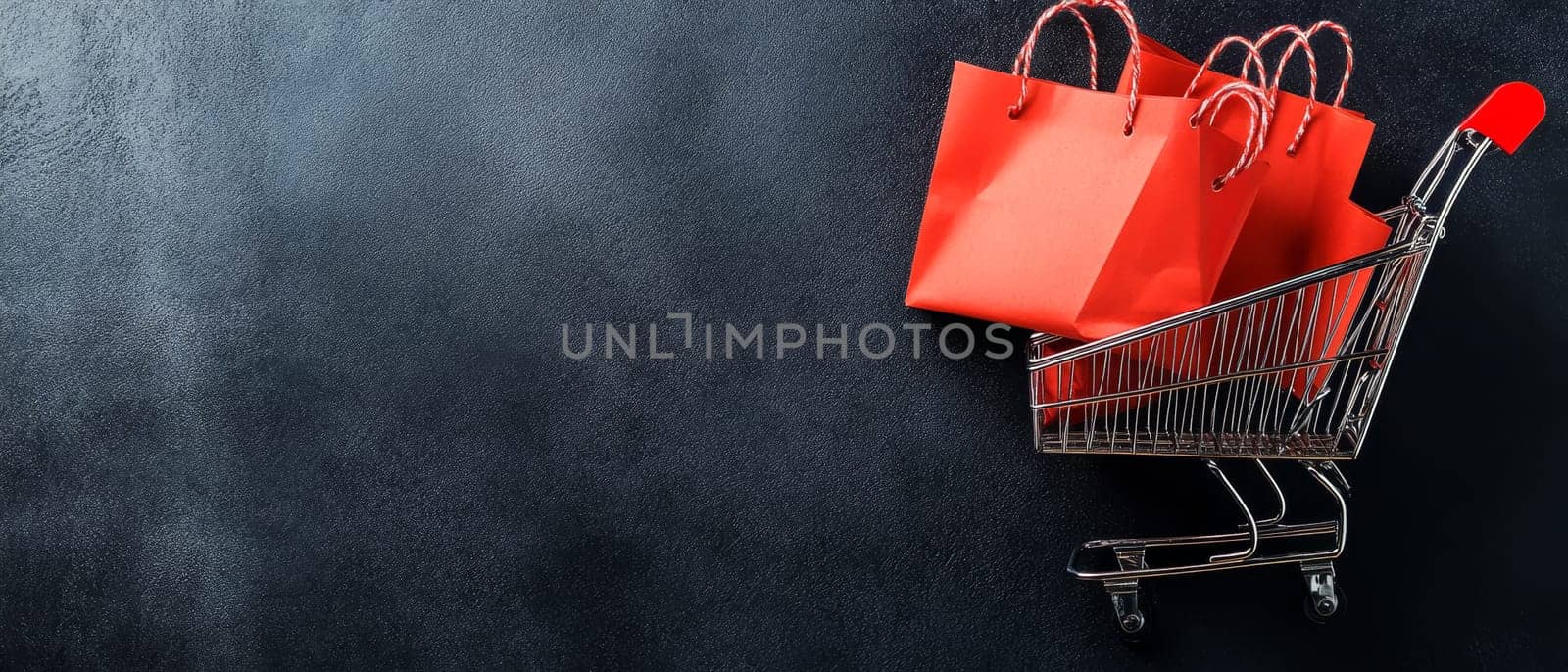 Miniature shopping cart containing red paper bags on dark textured background. Retail and e-commerce concept with copy space for Black Friday or sale.
