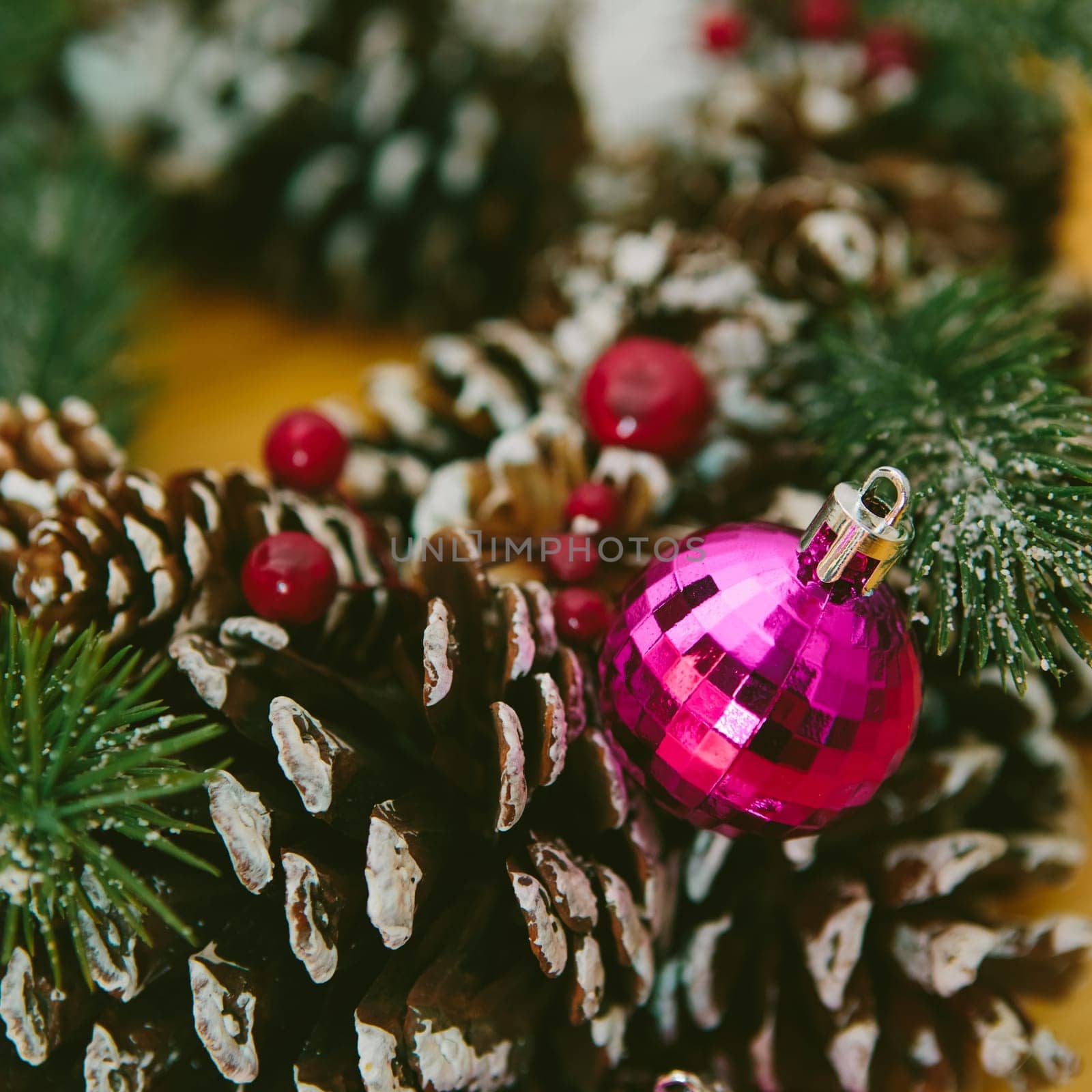 Christmas Decoration. Holiday wreath adorned with snow-dusted pine cones, evergreen branches, red berries, and shiny pink Christmas ornament