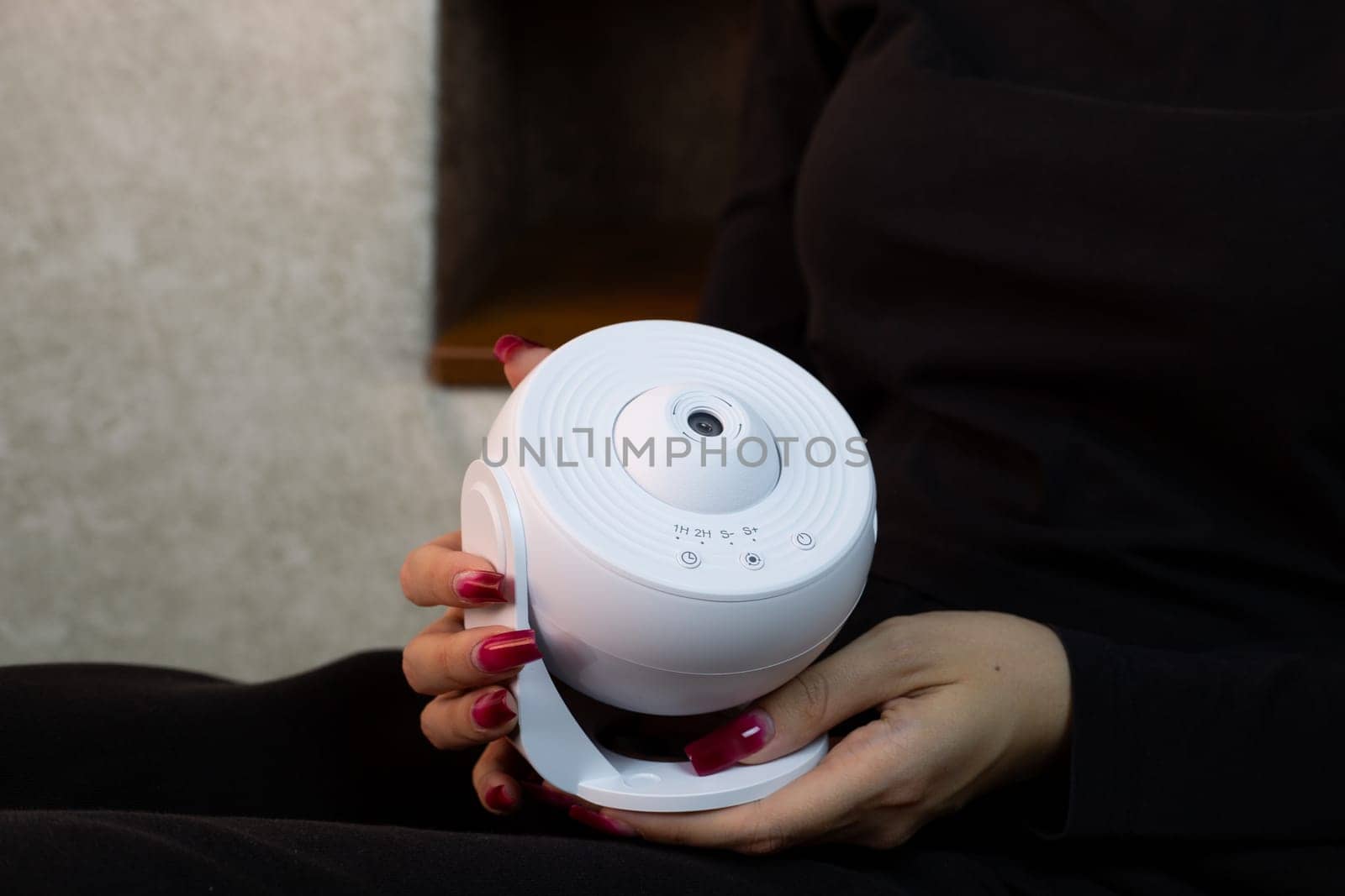 Girl holds in her hands galaxy projector for studying solar system and deep space, compact device for projecting starry sky onto ceiling of room