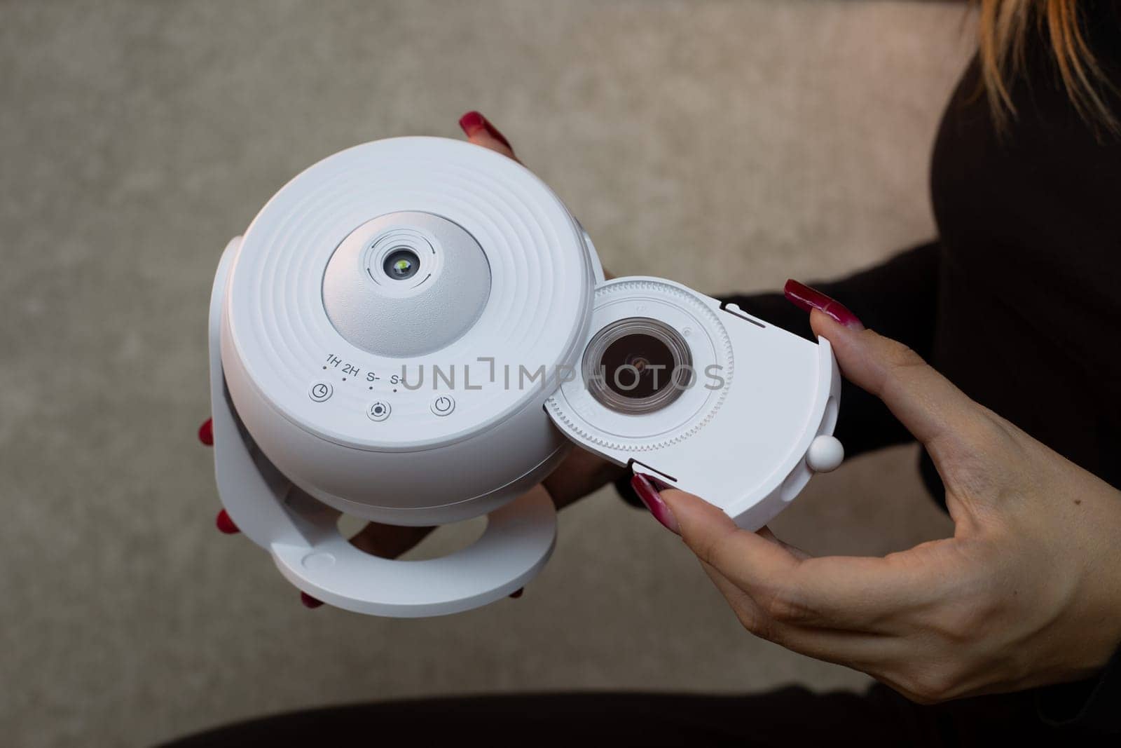 Girl inserts replaceable cartridge with images of planets and stars into galaxy projector for projection onto the ceiling of the room, home planetarium for exploring deep space