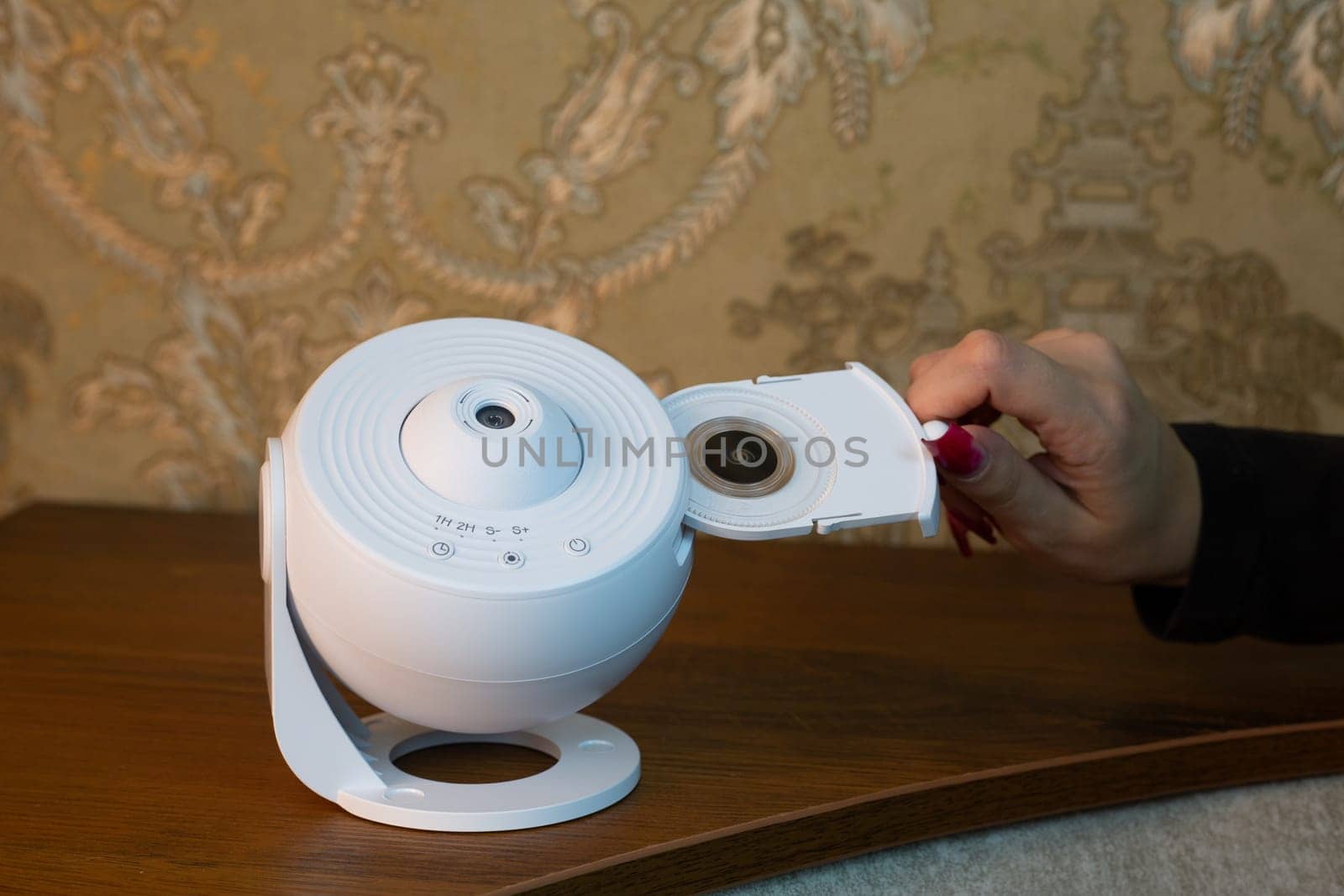 Female hand inserts galaxy image cartridge into compact home projector for space exploration, scientific device for home use, room projector on shelf