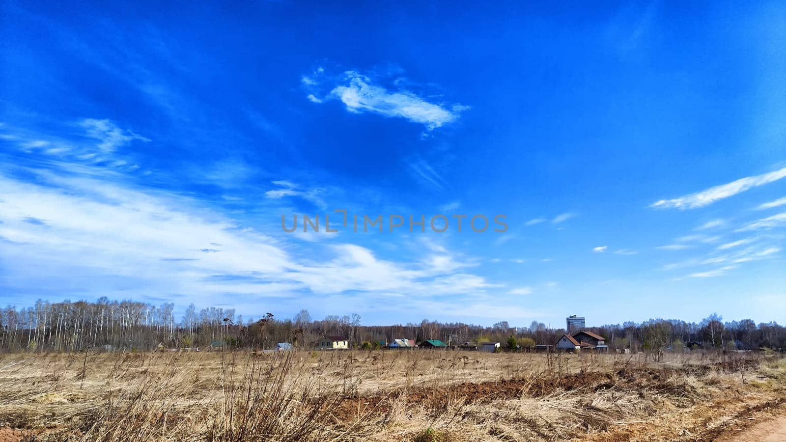 A vast field of dry yellow grass stretches towards a picturesque village, framed by a bright blue autumn sky