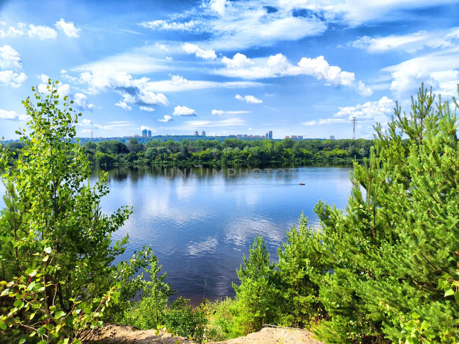 Bright sunlight reflects off the calm water, surrounded by lush greenery and picturesque clouds in the blue sky.