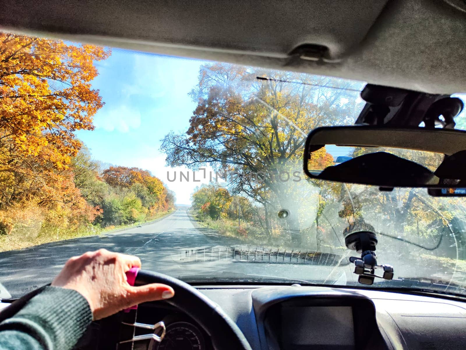 Car salon, windshield, hand of woman on steering wheel and landscape. View from seat of driver on nature at sunny day. Single trip of female traveler