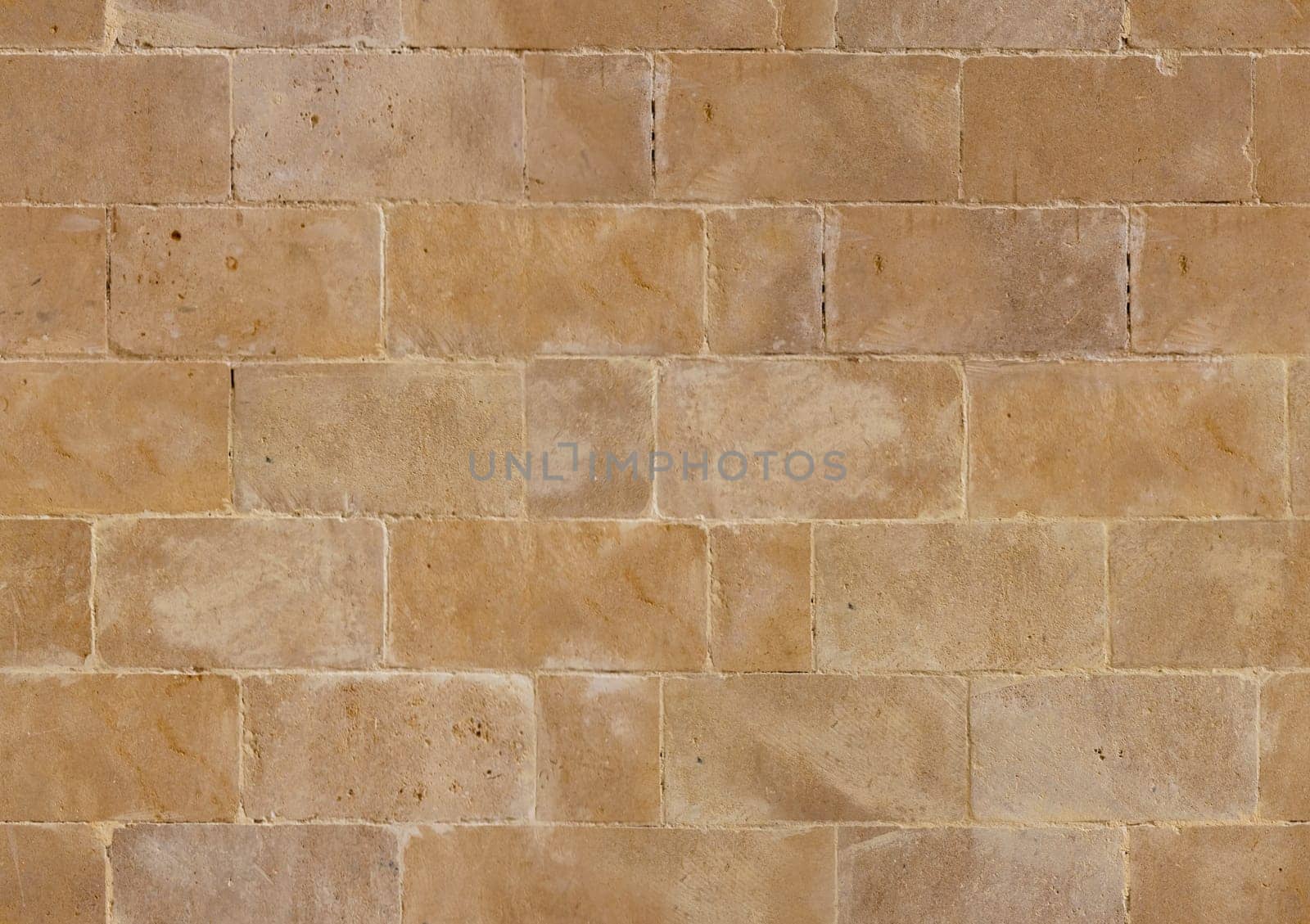 A detailed view of a seamless stone wall texture, showcasing its natural beige tones and subtle color variations. The rough surface provides a consistent, rustic background suitable for architectural use.