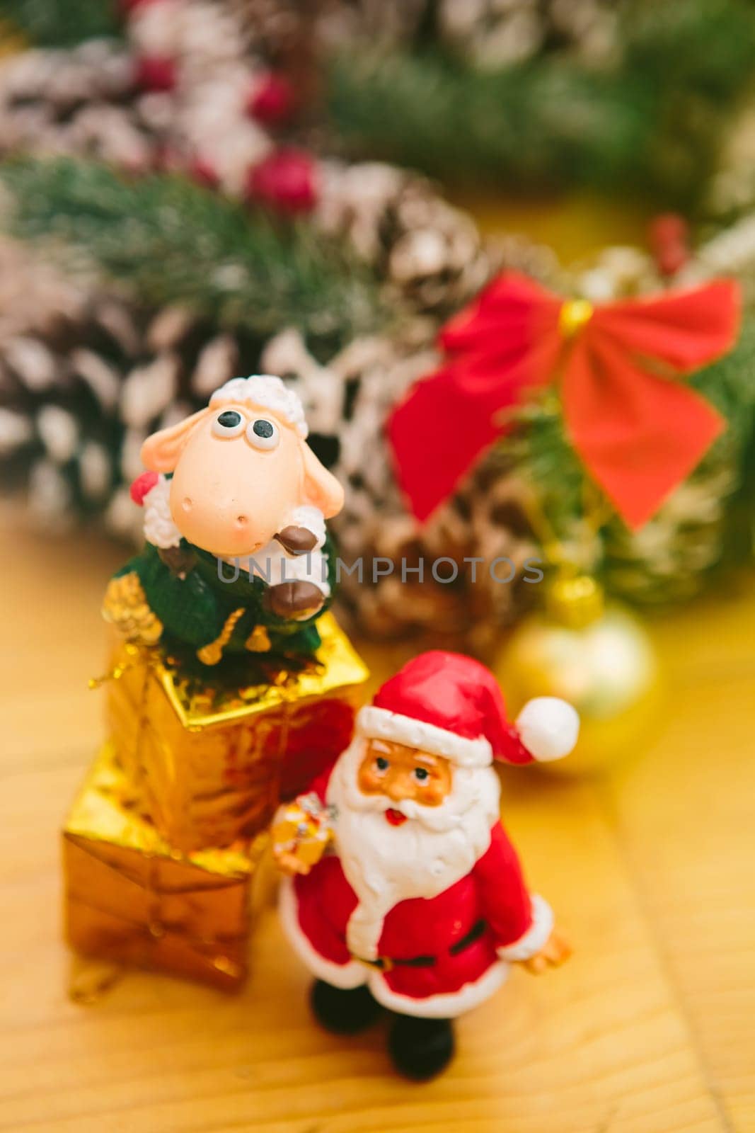 Christmas wreath decorated with pine cones, red bows, and evergreen branches sits on a wooden surface. In front of the wreath, a small Santa Claus figurine and golden ornaments add a cheerful holiday touch