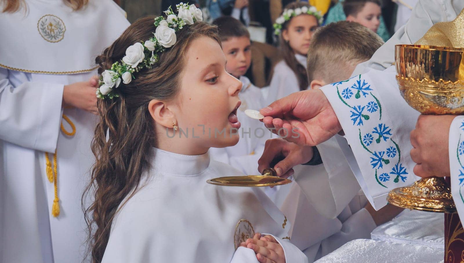Young girl wearing a white dress and floral wreath receiving her first holy communion