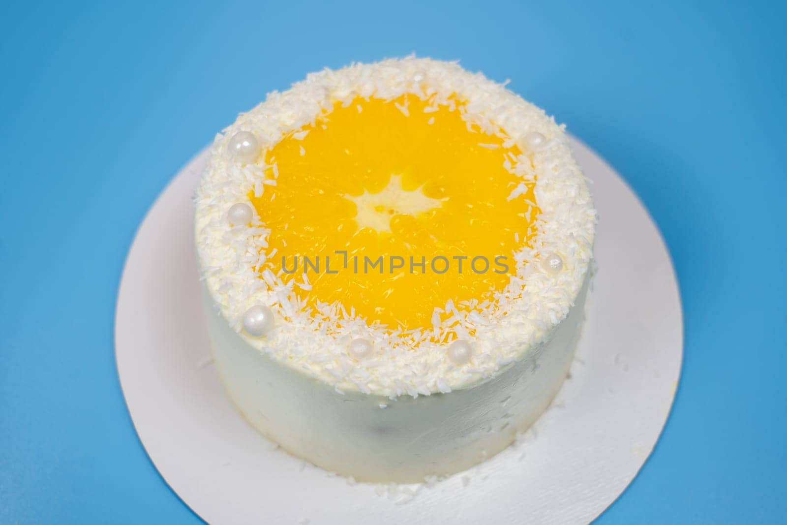 Delicious white cake decorated with orange and coconut flakes standing on white plate on blue background