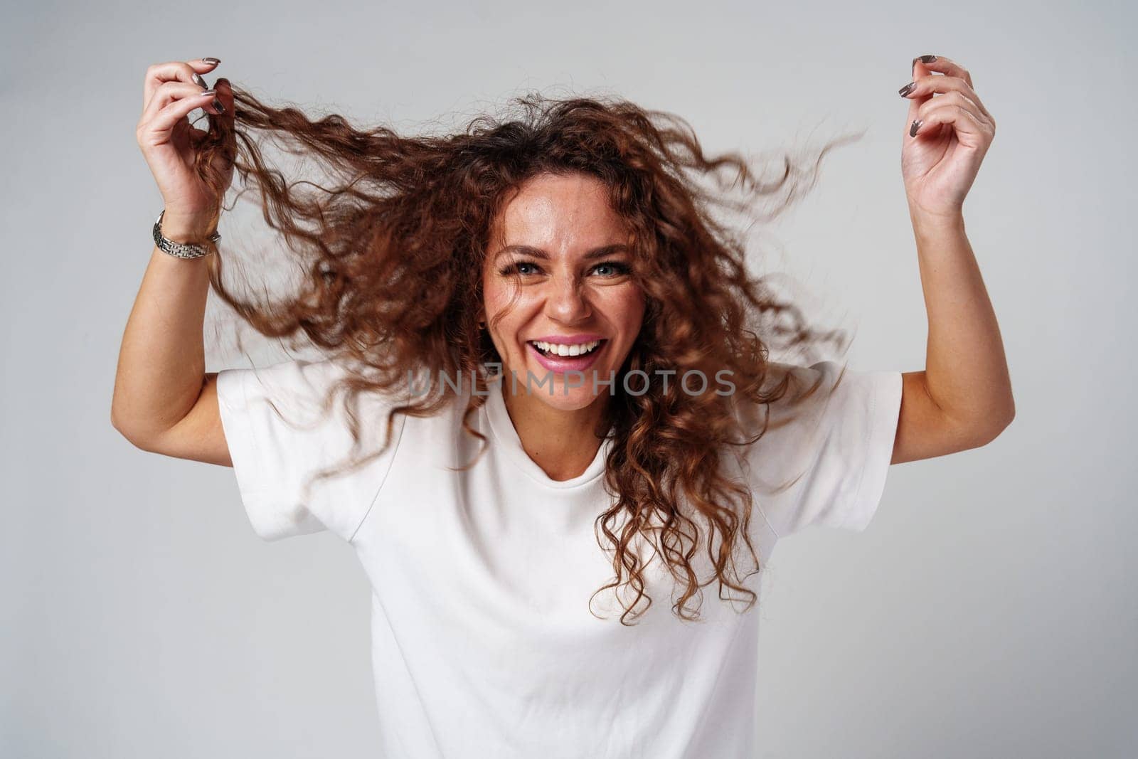 A woman in a white shirt and ripped jeans posing positively with a playful expression in a light studio setting close up