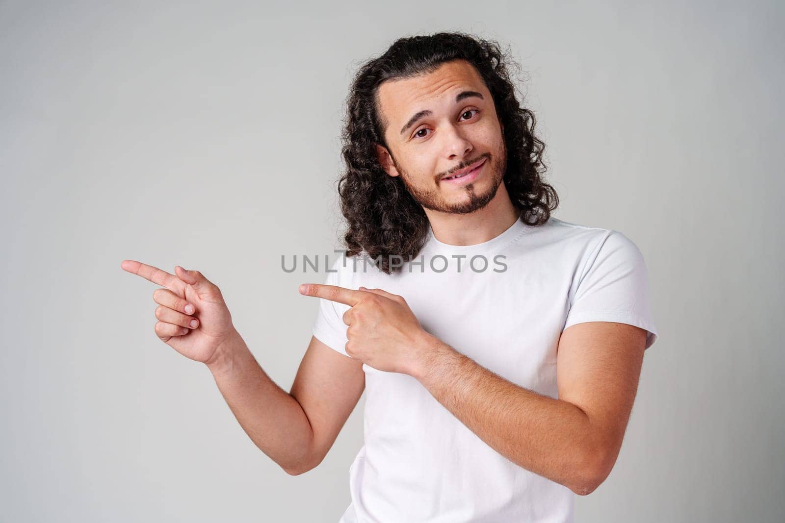 Young man in a white t-shirt and jeans pointing confidently while smiling in a studio setting close up