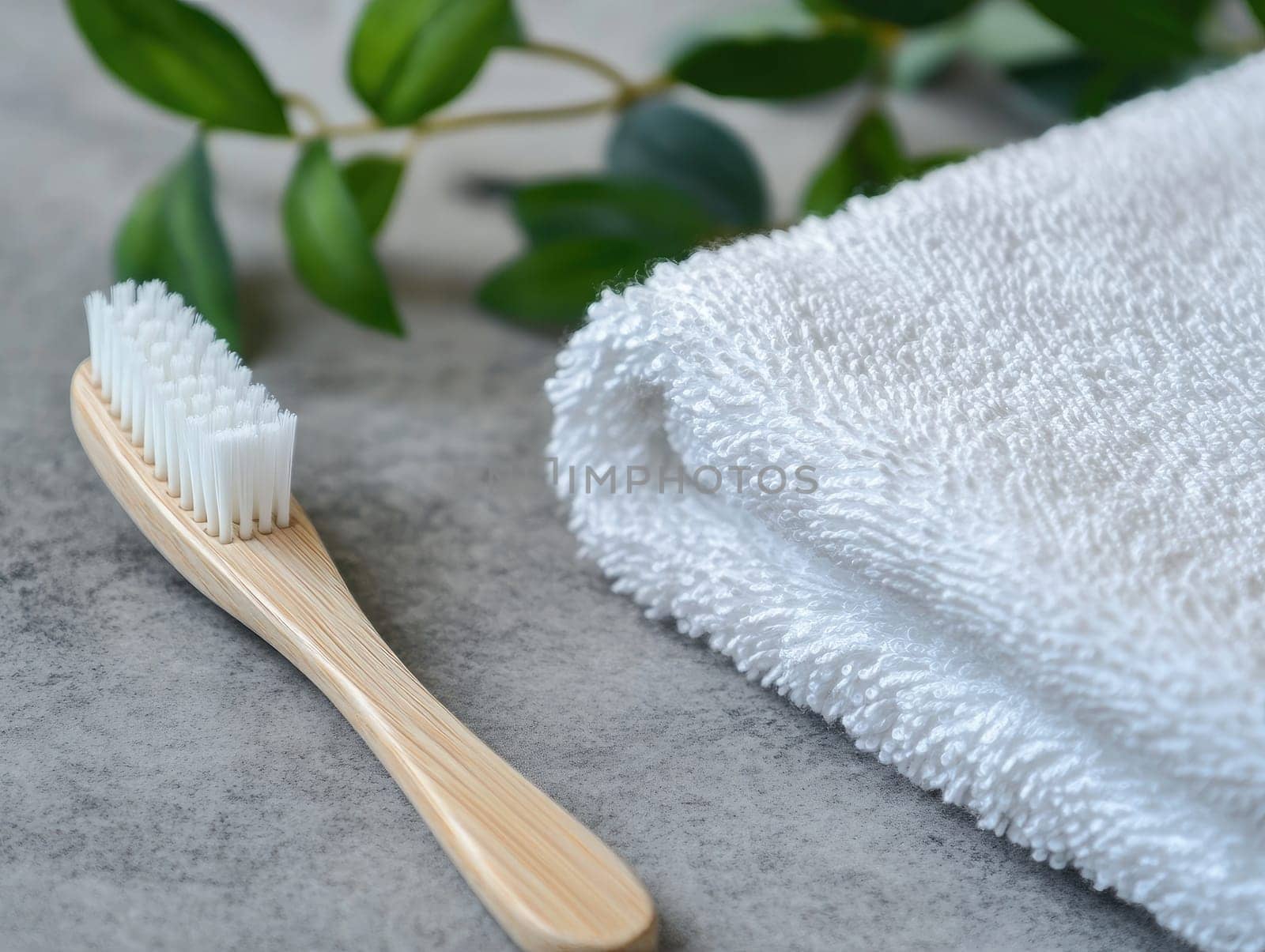A wooden toothbrush rests next to a fluffy white towel with green leaves in the background, creating a calming and hygienic atmosphere for personal care.