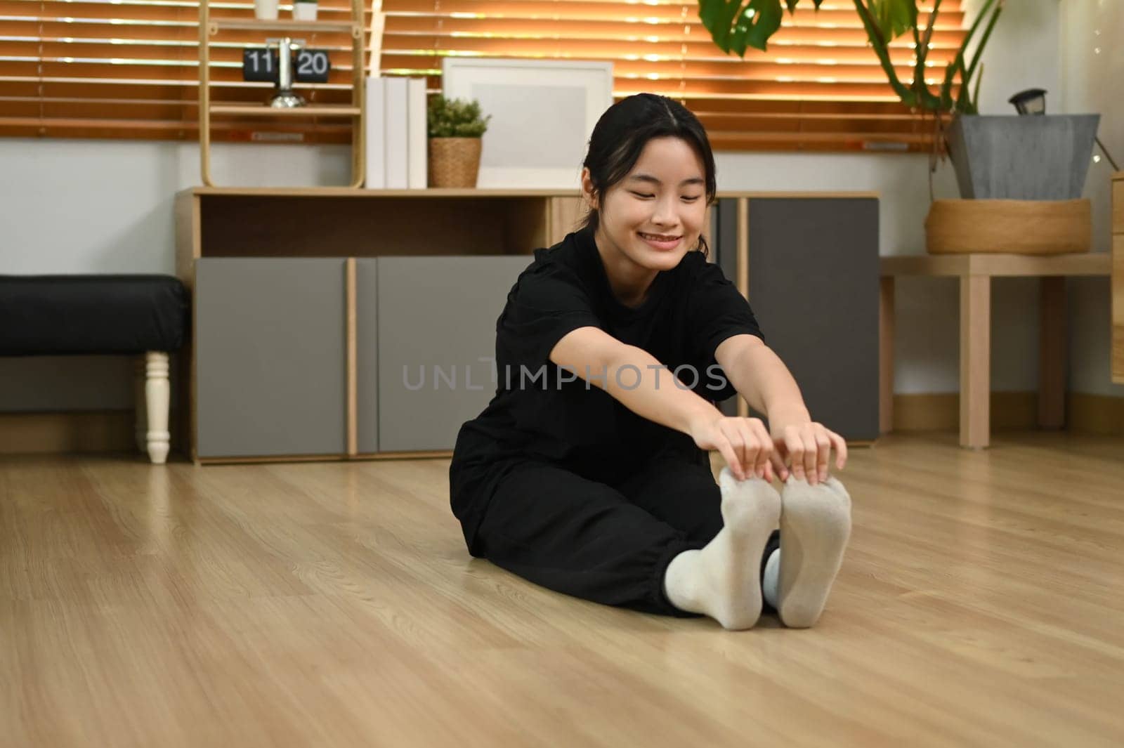 Smiling asian girl stretching her legs on floor getting ready for workout at home.