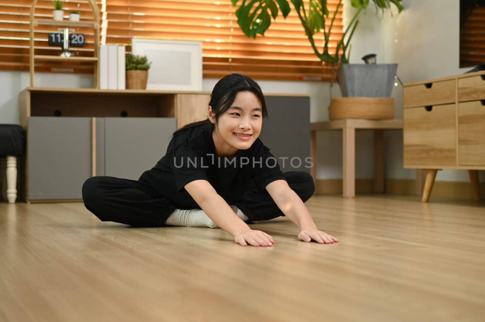 Pretty asian girl stretching on wooden floor getting ready for workout at home.