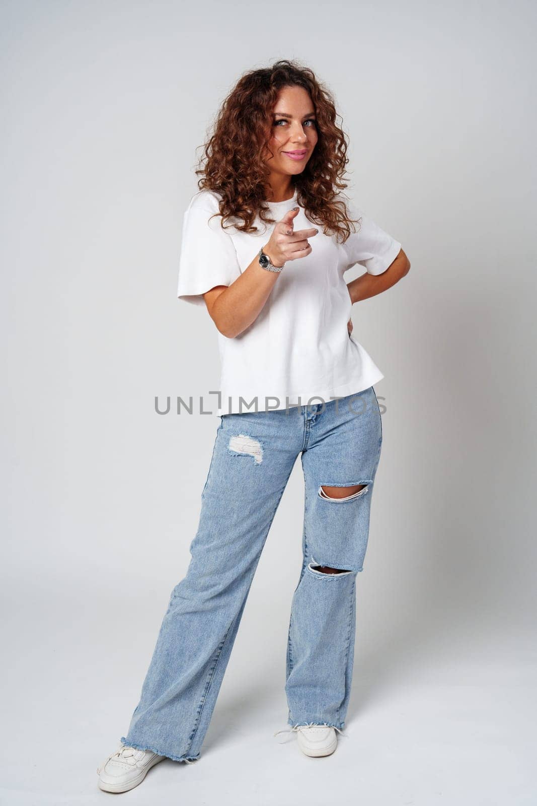 A young woman with curly hair playfully points towards the camera in a bright studio setting