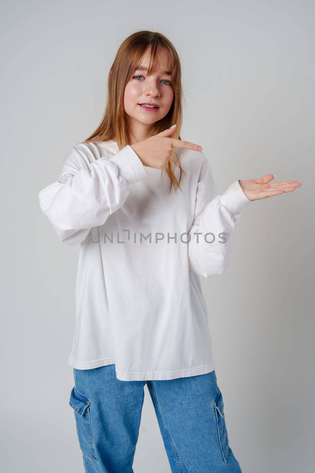 Young girl happily pointing against a neutral background while wearing a cozy white sweatshirt close up