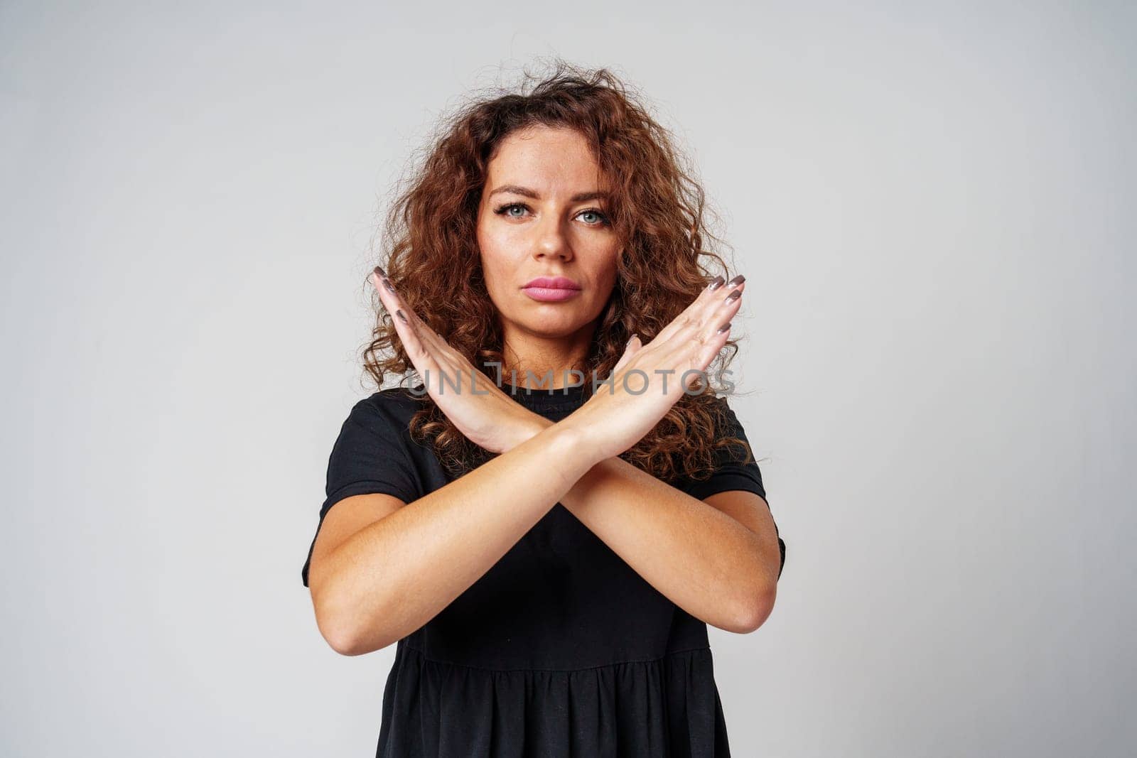 Woman in a black dress standing against a gray background with arms crossed close up