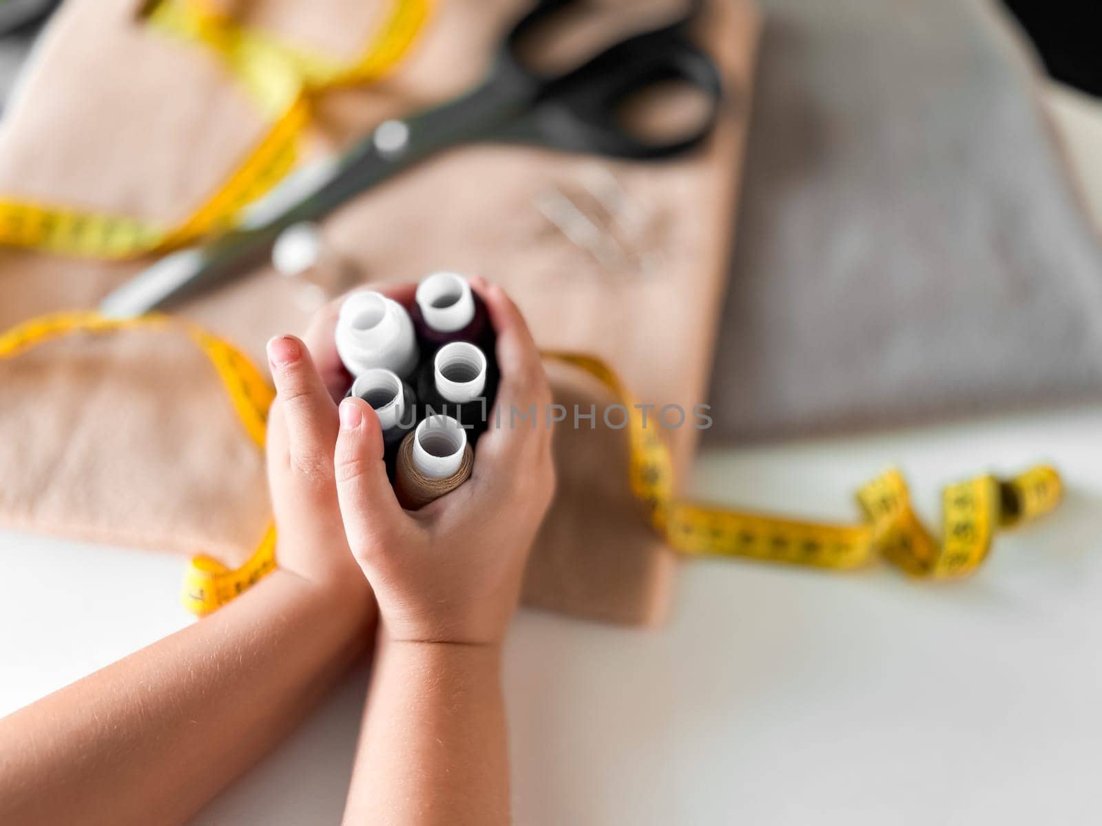Hands holding sewing threads with scissors and measuring tape in tailoring setup.