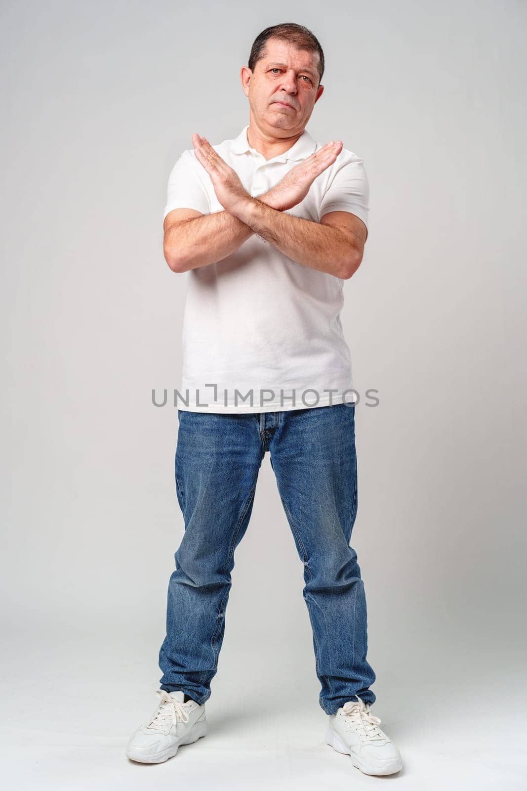 A man making a gesture of refusal with arms crossed against a light background in studio
