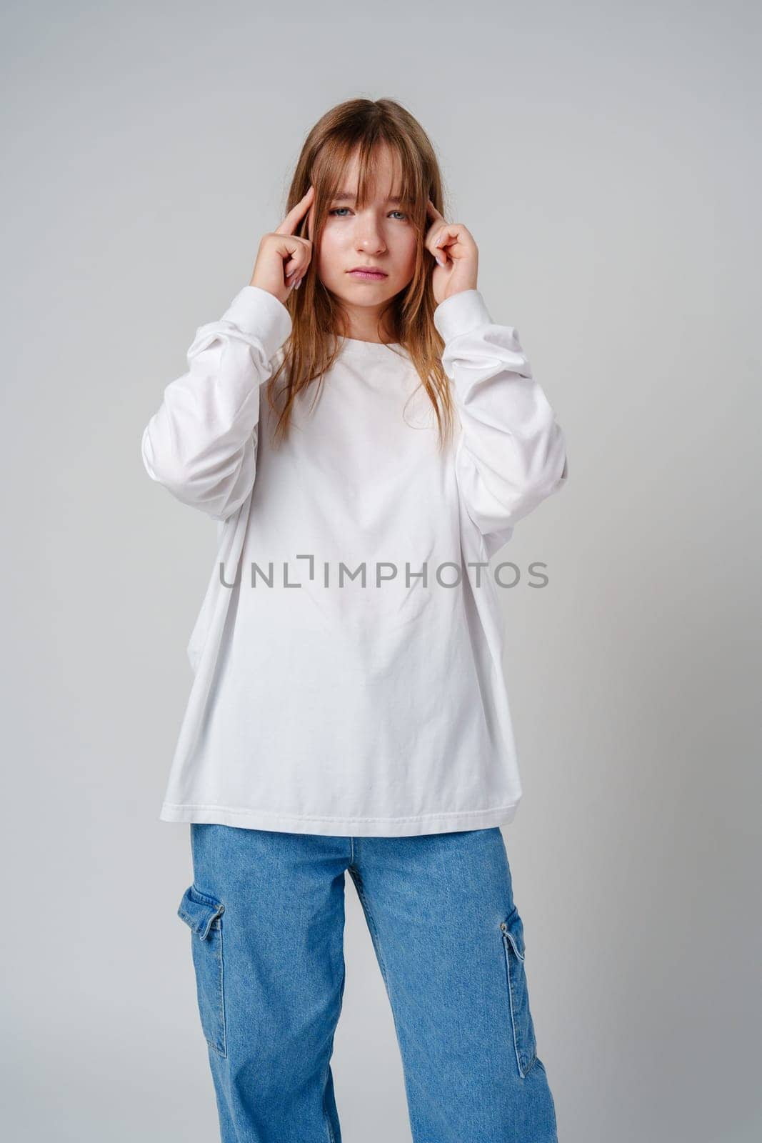 Young girl in a white sweater holding her head in discomfort against a minimalist background close up