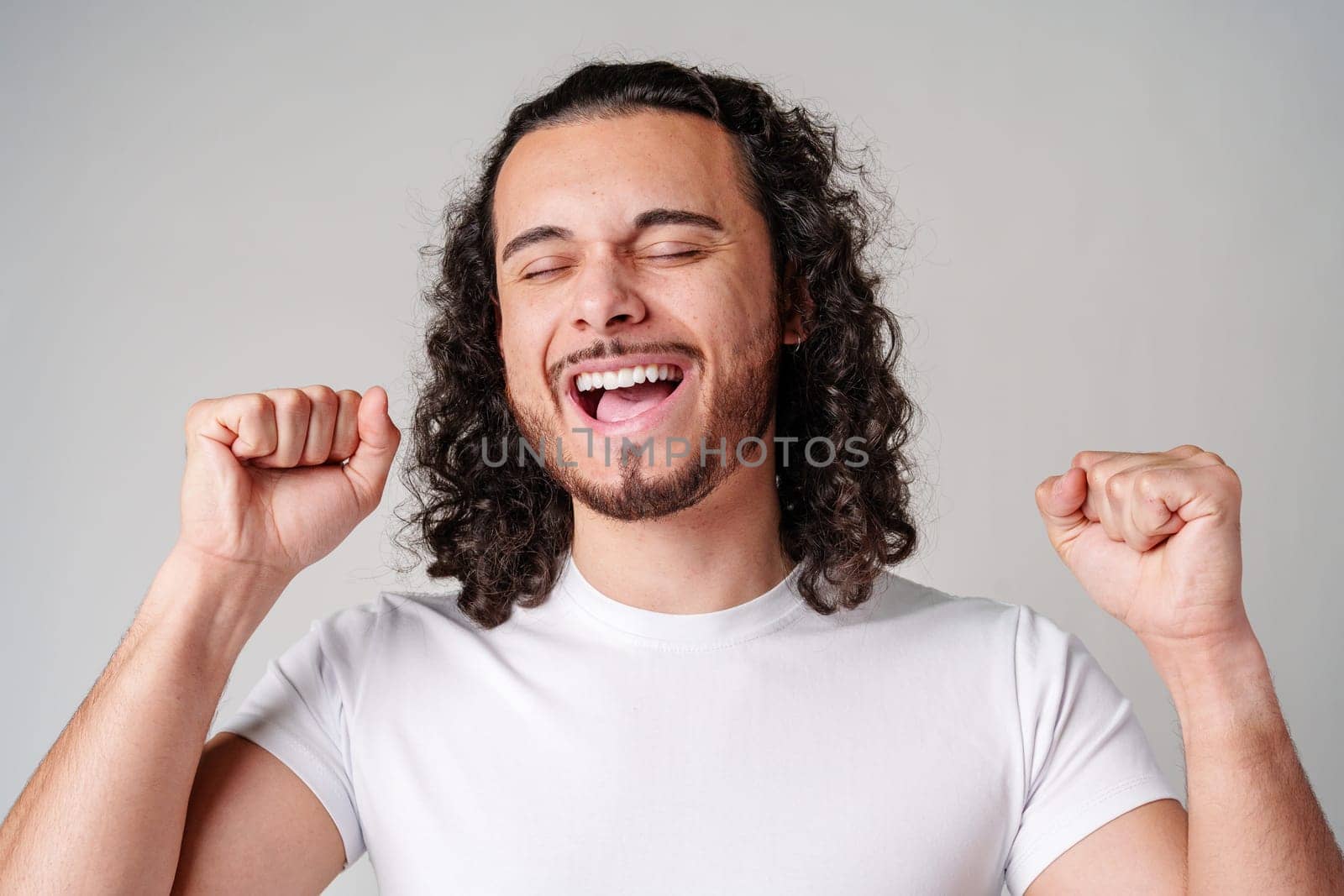 Happy man celebrating success with raised fists in a studio against a plain background close up