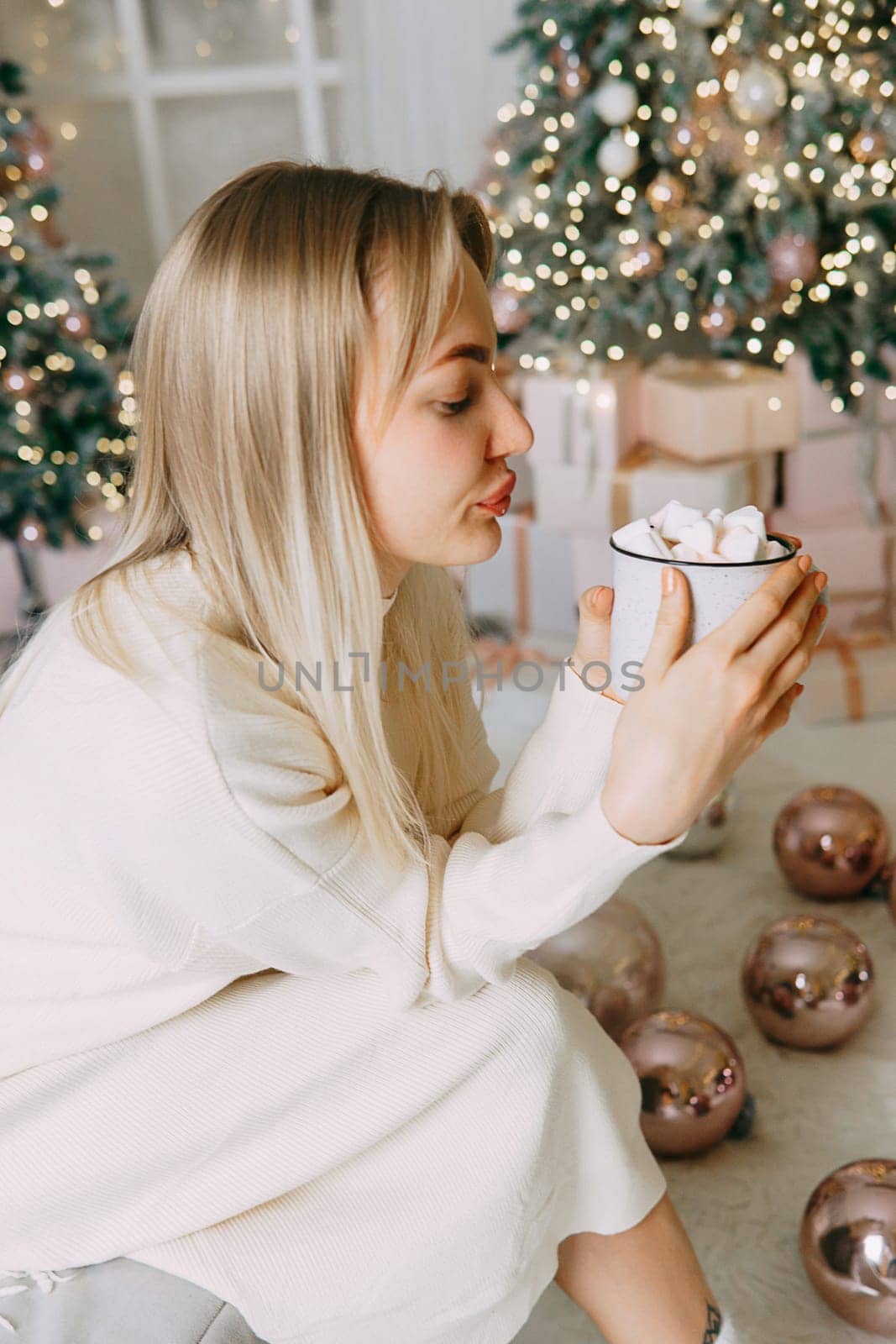 Blonde in a bright Christmas interior with a cup of hot drink with marshmallows. New Year's interior in pink tones. The winter holidays period.