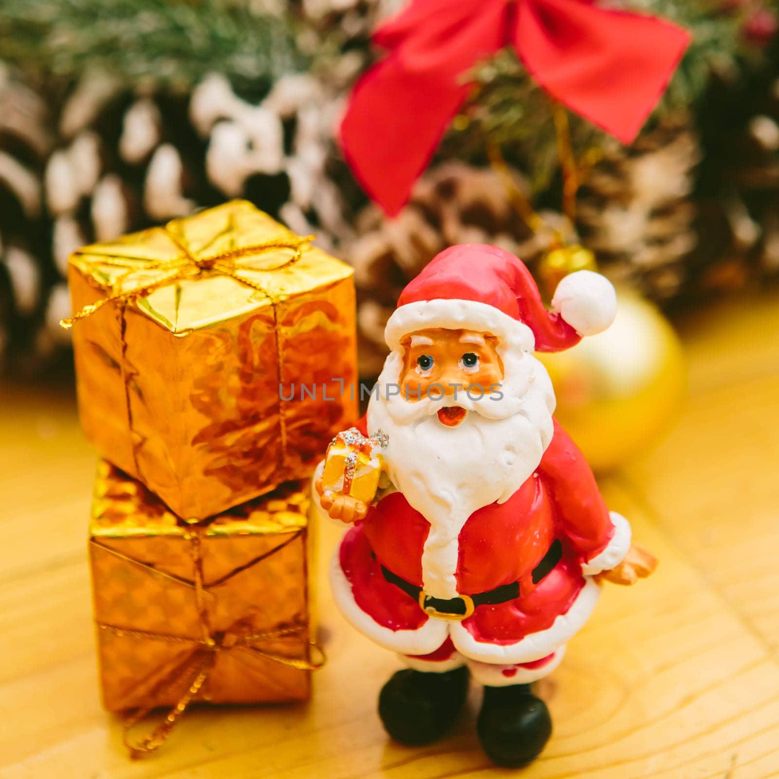 Christmas wreath decorated with pine cones, red bows, and evergreen branches sits on a wooden surface. In front of the wreath, a small Santa Claus figurine and golden ornaments add a cheerful holiday touch