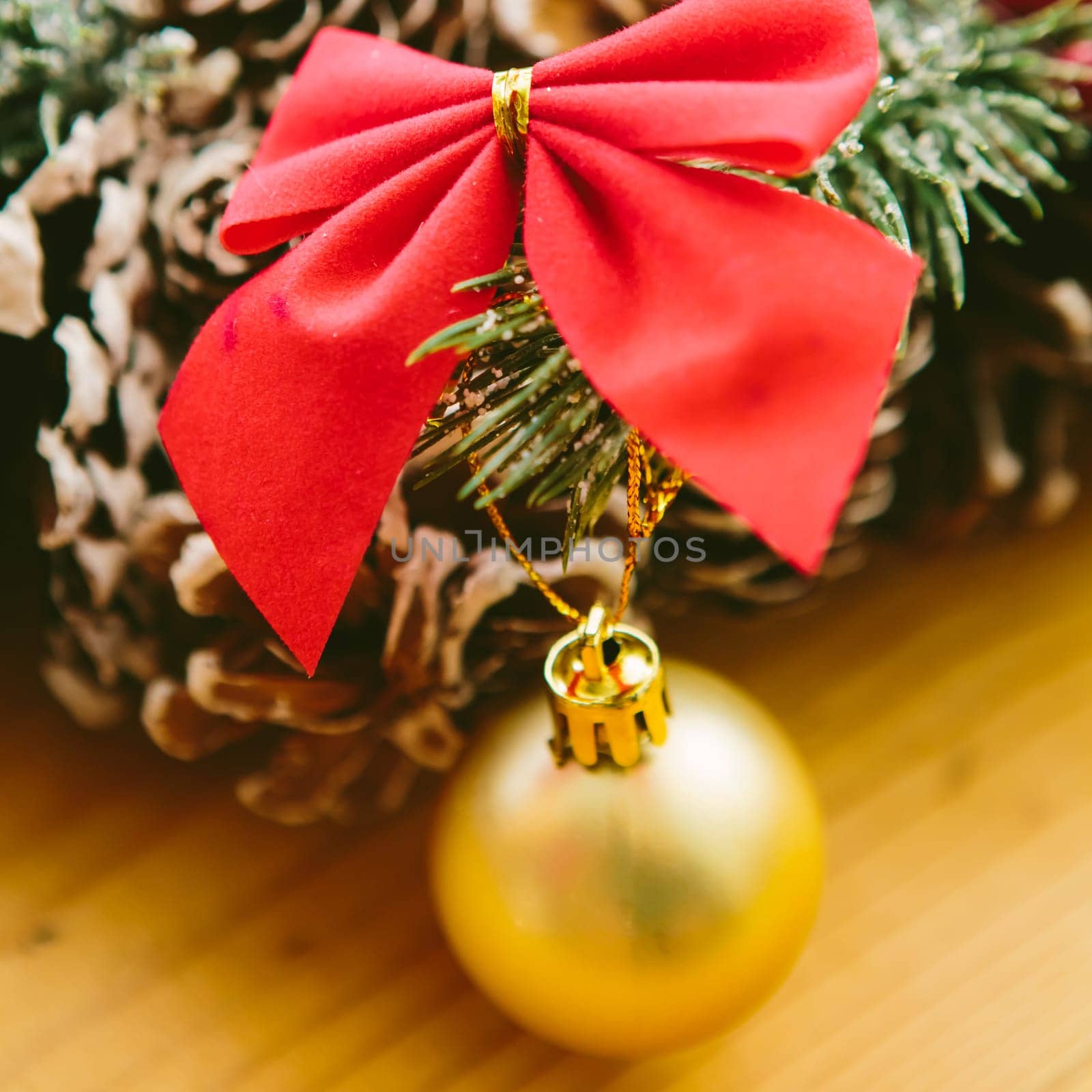 Christmas Decoration. Christmas wreath made of pine cones, decorated with red bows, evergreen branches, and gold ornaments, sits on a wooden surface.