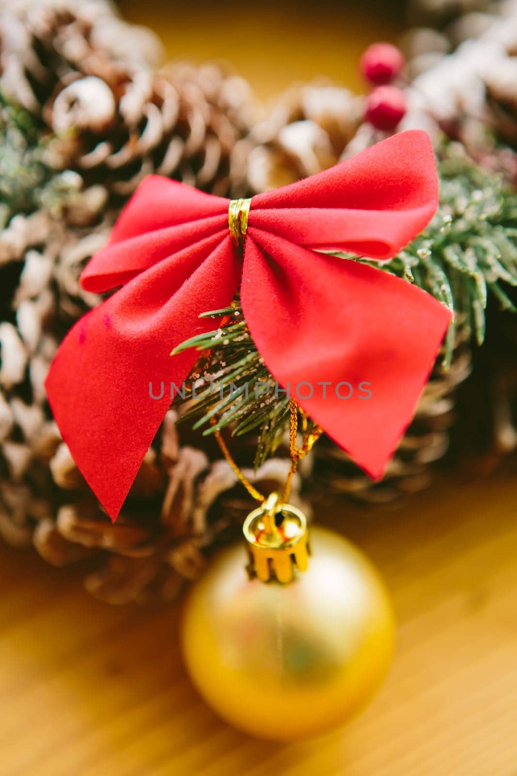 Christmas Decoration. Christmas wreath made of pine cones, decorated with red bows, evergreen branches, and gold ornaments, sits on a wooden surface.