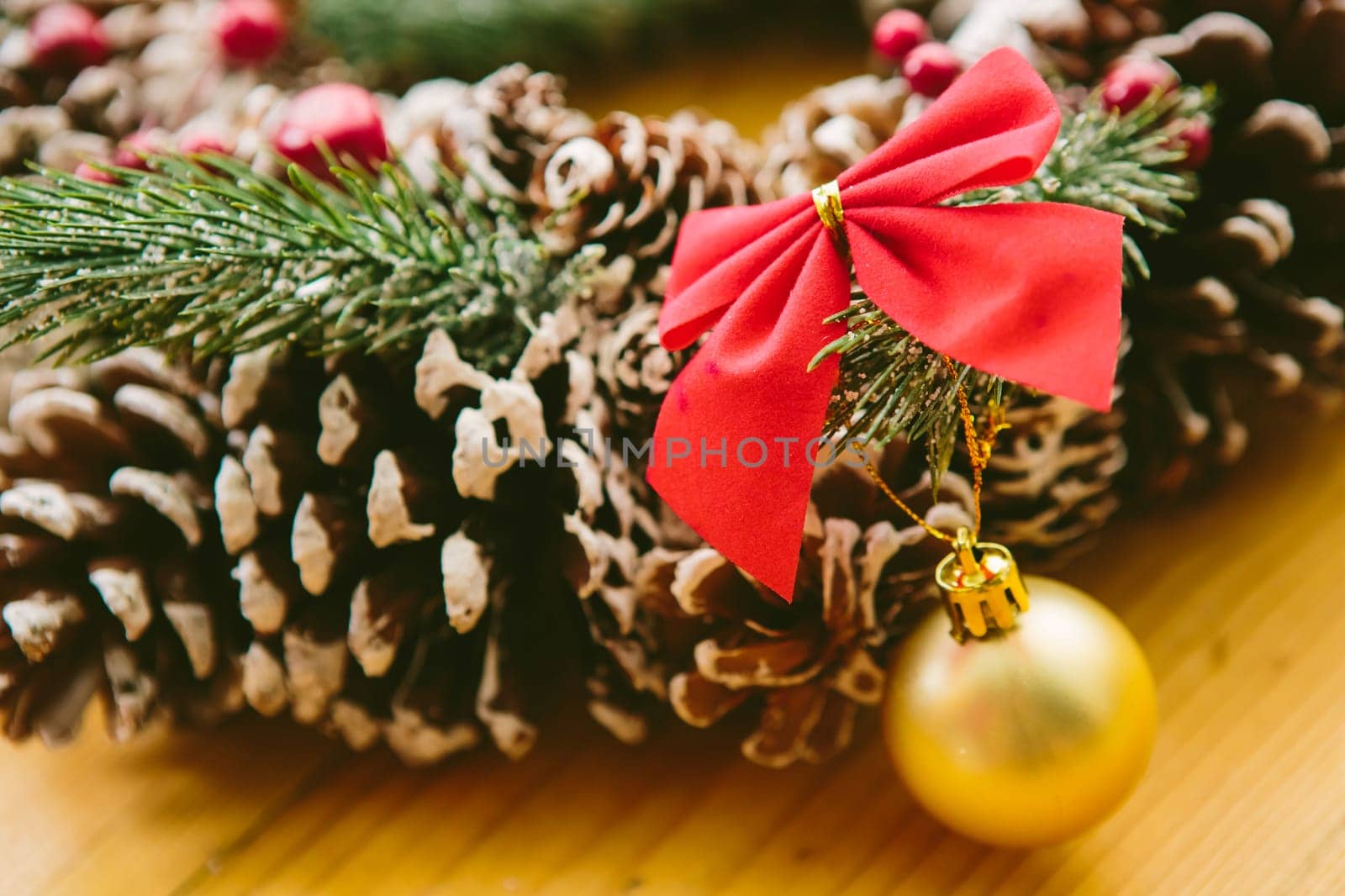 Christmas Decoration. Christmas wreath made of pine cones, decorated with red bows, evergreen branches, and gold ornaments, sits on a wooden surface.
