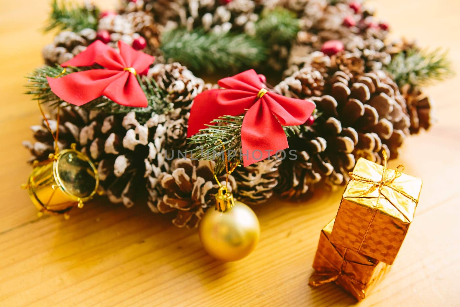 Christmas Decoration. Christmas wreath made of pine cones, decorated with red bows, evergreen branches, and gold ornaments, sits on a wooden surface.