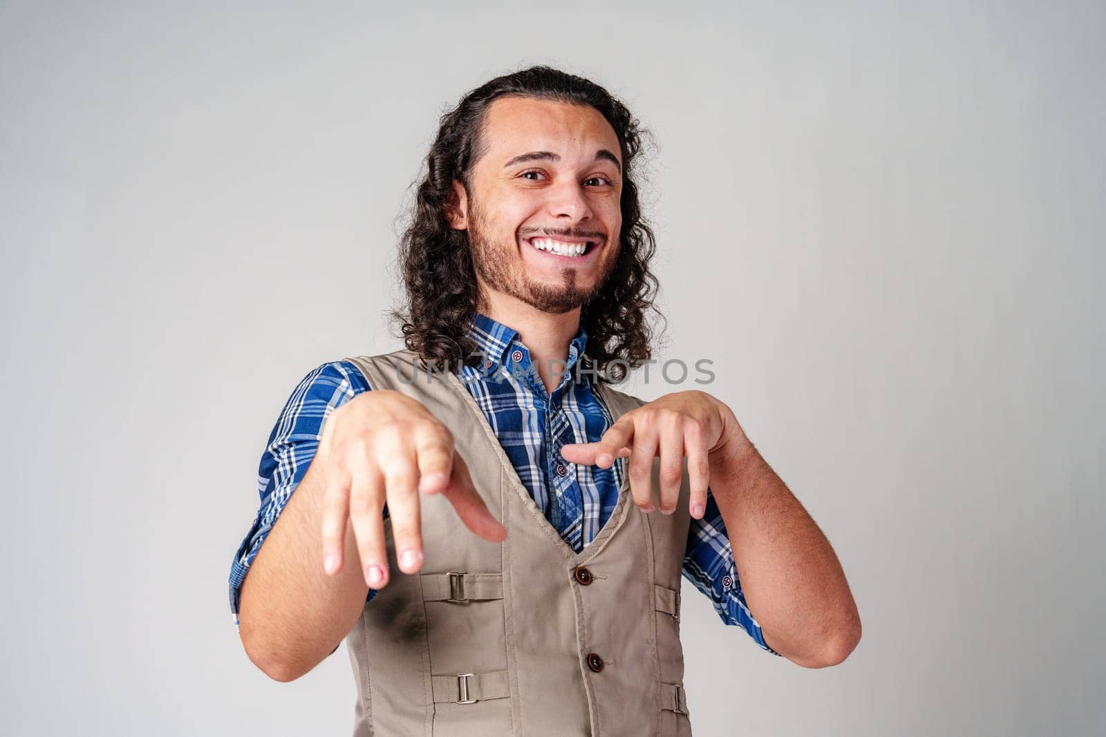 A cheerful man with curly hair makes playful gestures against a neutral background close up