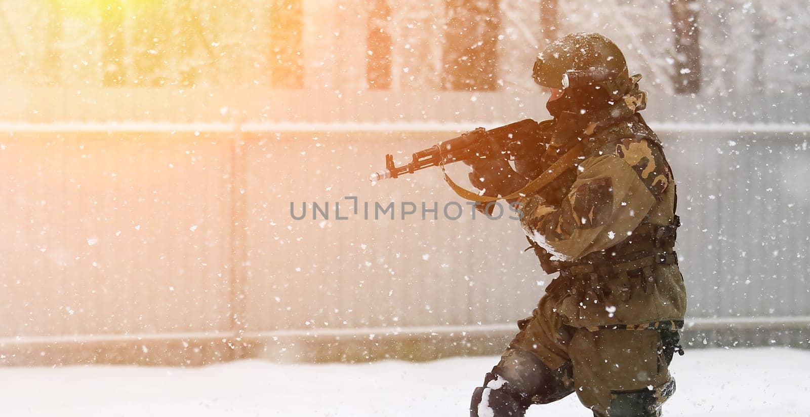 A soldier wearing a mask and winter camouflage uniform is pictured advancing through the snow while holding a gun. The soldier is likely participating in a military operation or training exercise.