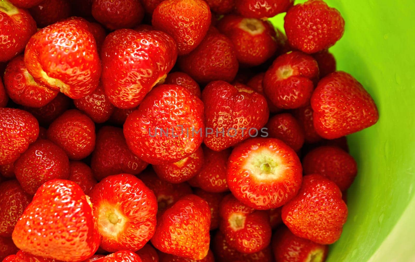 Sun-kissed strawberries, freshly picked and arranged beautifully, sit in a vibrant green bowl, radiating summer's warmth