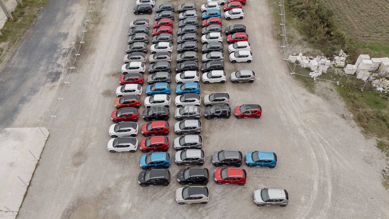 Capturing a busy parking lot from above, shiny new cars await delivery at a distribution center, showcasing the vibrant automotive industry