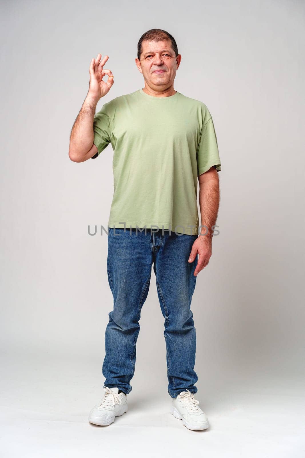 A man with a slight smile making an OK hand gesture against a neutral background close up